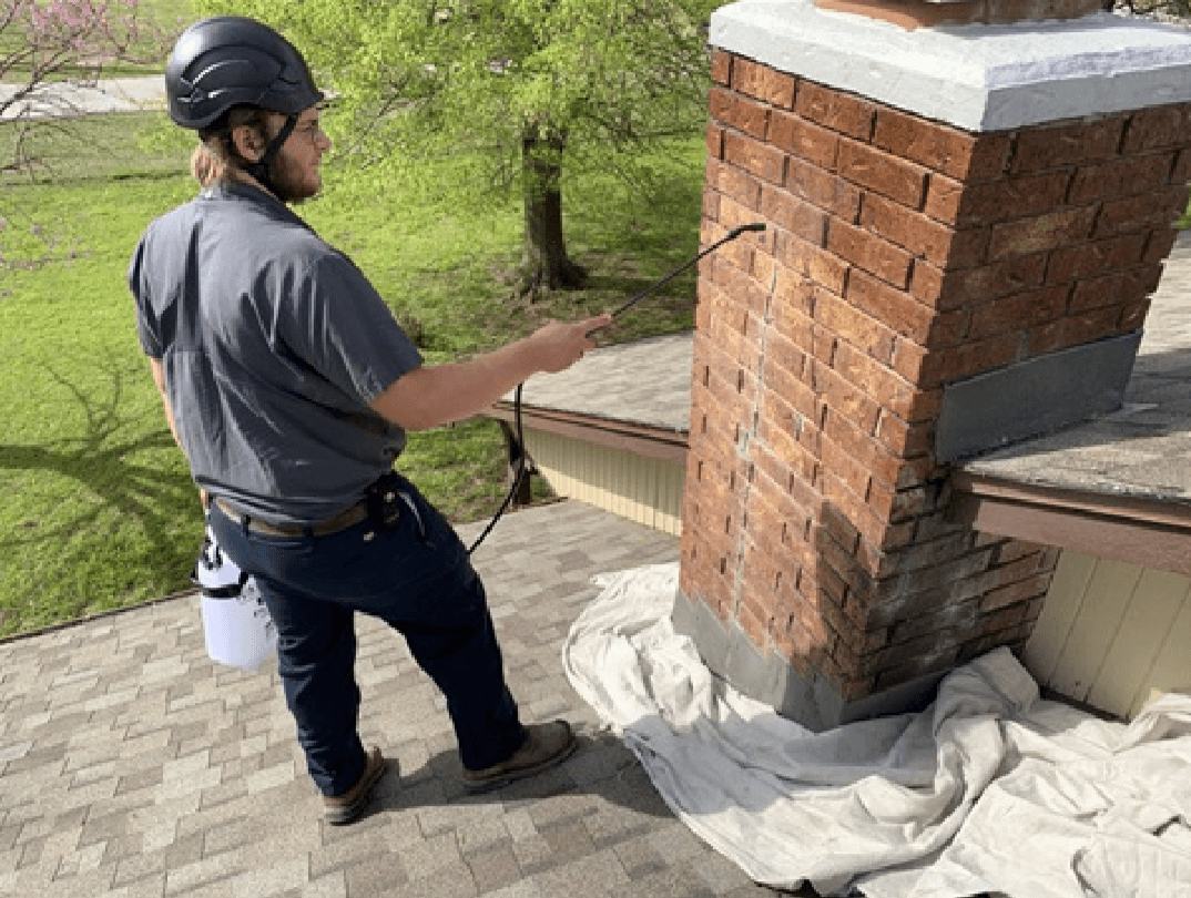 Technician Applying Water Repellent To Chimney with drop cloth at bottom of chimney and trees in background