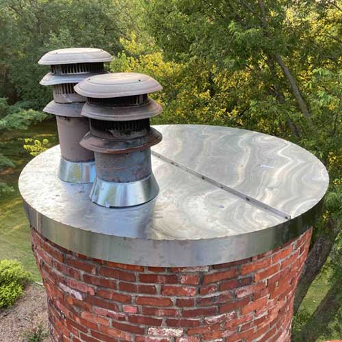 Round red brick chimney with stainless steel crown and two caps that need replacing