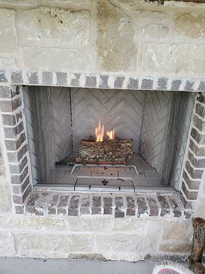 Outdoor Fireplace with small fire with brick around the firebox and stone surround