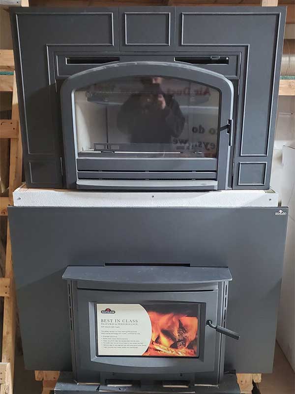 Two wood inserts on display - top stove has arched door with the man taking the picture reflection and bottom one has rectangular door - Napoleon